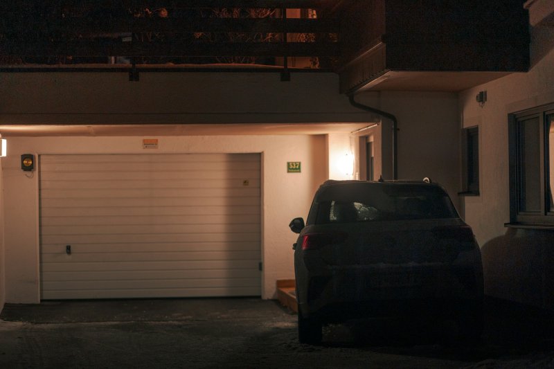 SUV in a driveway after dark in front of a residential garage door, lit by porch light — the after-hours scenario where emergency surcharges and pressure tactics kick in