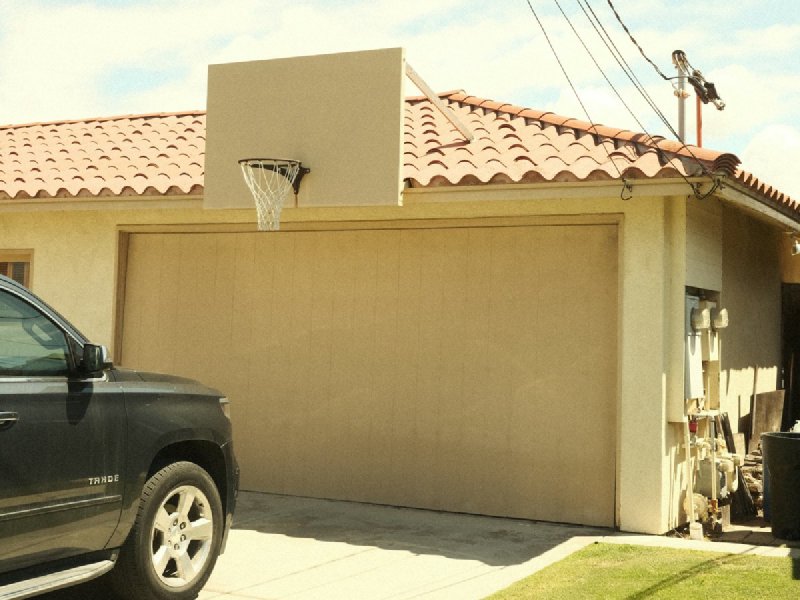 Black pickup truck parked on a concrete residential driveway in front of a single-story house with a beige garage door