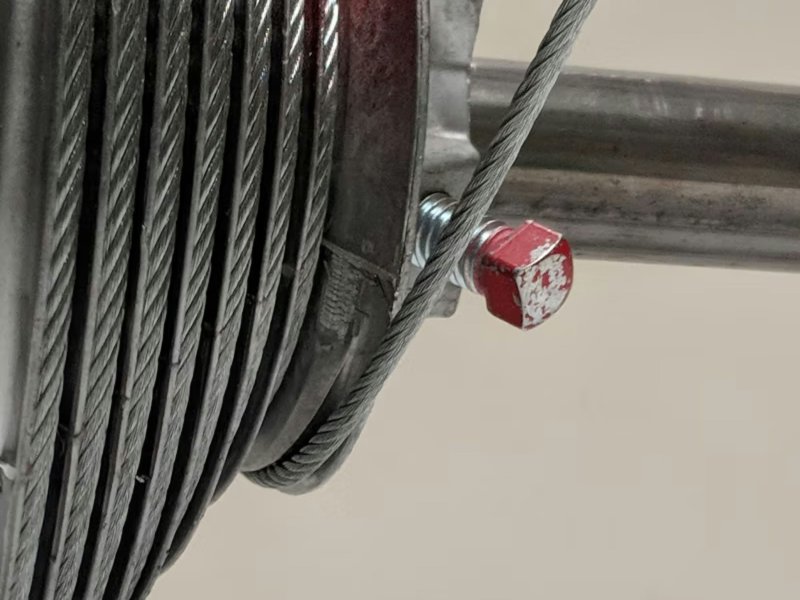 Close-up of a galvanized steel lift cable wrapped around a bolted drum component