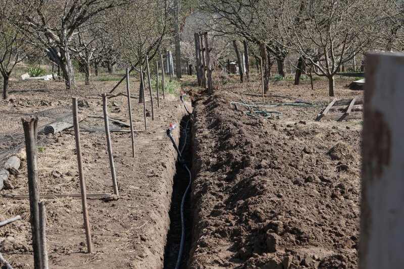 Long open trench with perforated drainage pipe laid in dirt, ready for gravel backfill