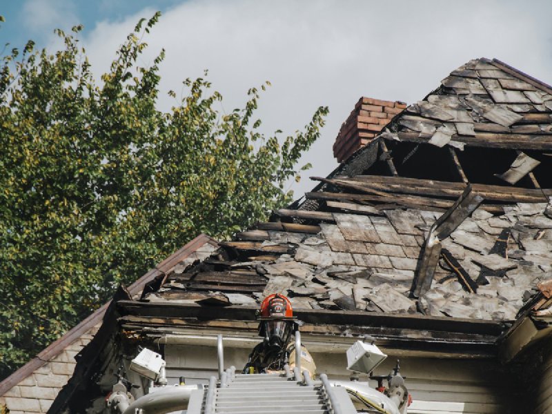 Firefighter on an extended aerial ladder working near the charred and damaged roof of a residential house
