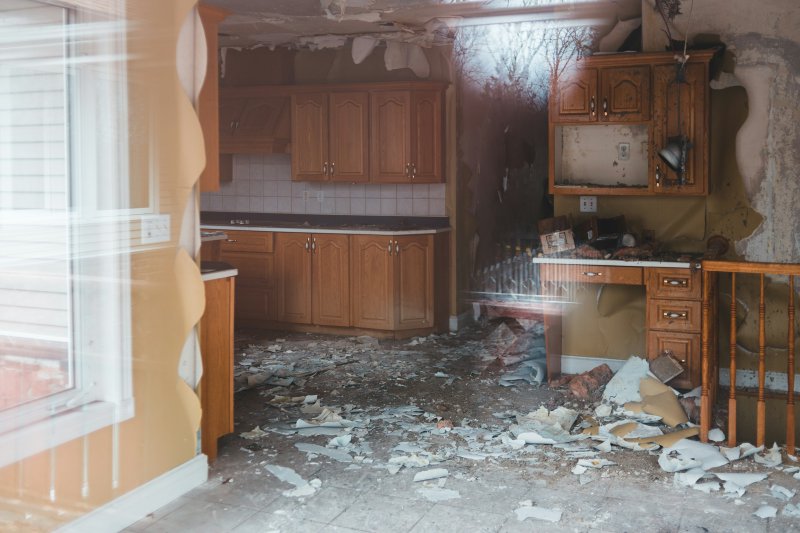 Residential kitchen after a fire with broken walls, scattered debris, and damaged wooden cabinets — the protein-smoke scope where enzymatic deodorization and full HVAC cleaning are mandatory