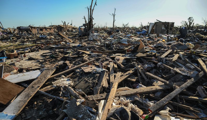 Wide swath of storm wreckage with splintered wood beams, broken furniture, insulation, and household debris piled where homes once stood