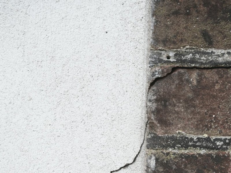 Diagonal crack running across the junction of a white plaster wall and an exposed brick wall