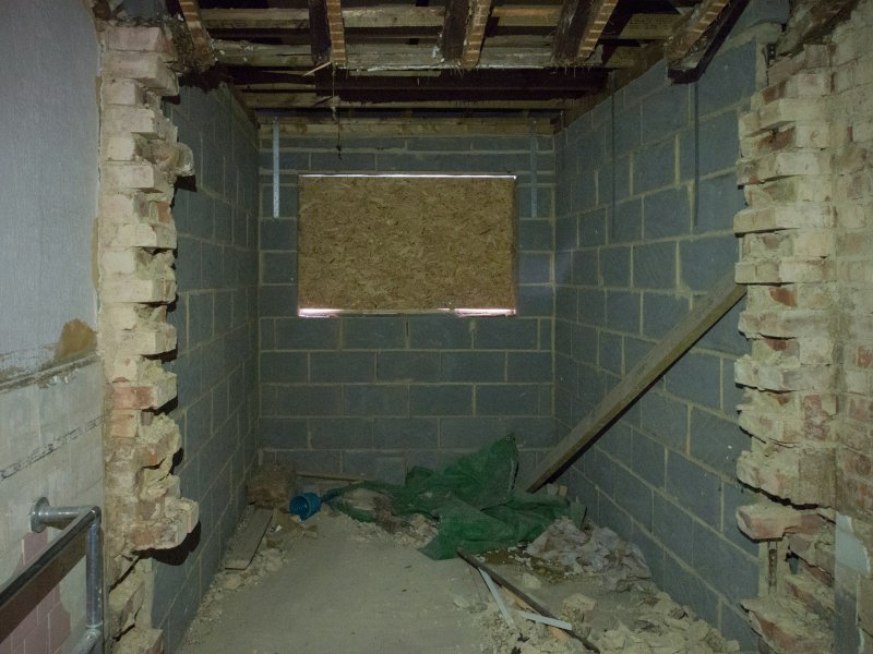 Narrow unfinished basement with exposed brick walls, concrete block sections, and a boarded-up window