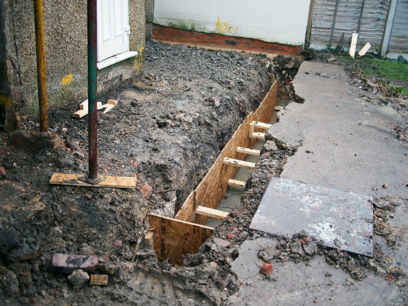 Excavated trench with wooden formwork next to a concrete foundation wall