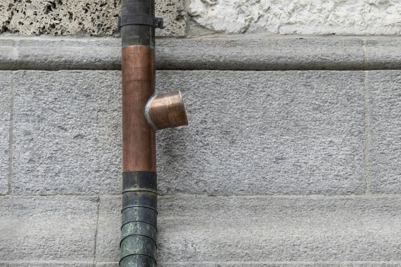 Vertical copper pipe with elbow joint, oxidized green patina at the lower end