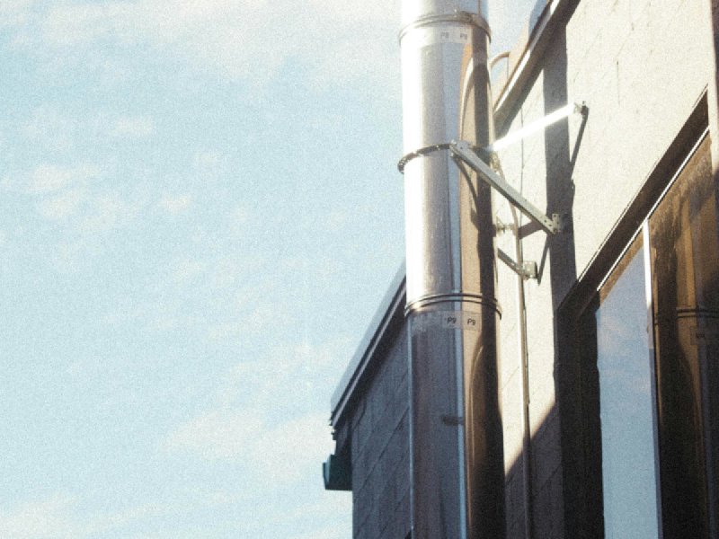 Vertical metal vent pipe rising past a building's roofline against the sky