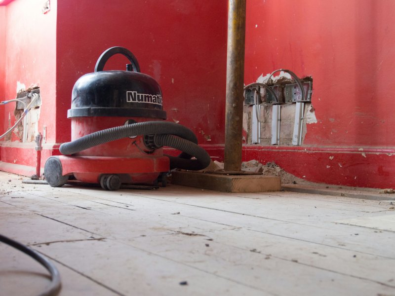 Numatic wet-dry extraction vacuum staged in a residential room mid-restoration with exposed wiring on the wall