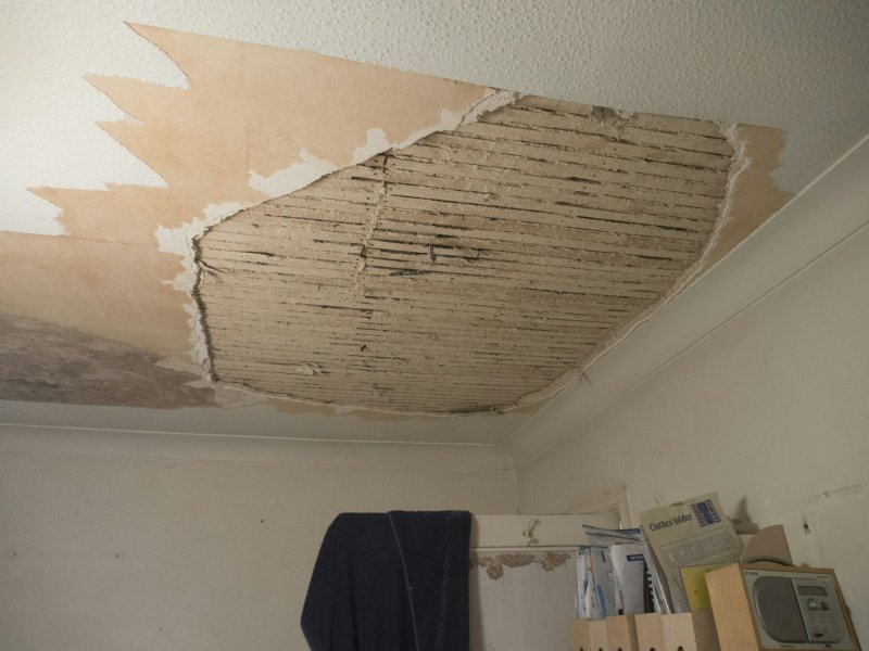 Severely damaged ceiling with drywall peeled back and water-stained wooden beams exposed