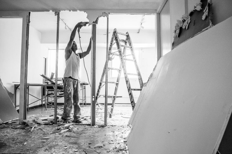 Worker using a drill to remove water-damaged drywall during restoration demolition