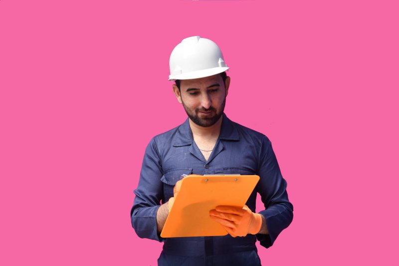 Construction worker in white hard hat and orange gloves holding an orange clipboard, illustrating the daily drying-log documentation that closes out a mitigation job