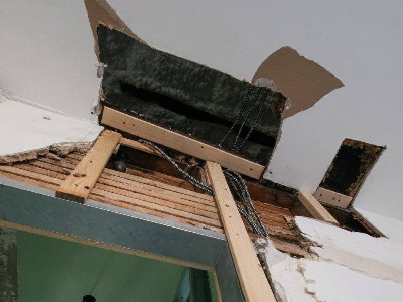 Exposed ceiling cavity with damaged drywall and visible wooden beams, illustrating the kind of hidden saturation discovered mid-cycle that drives supplemental drying days