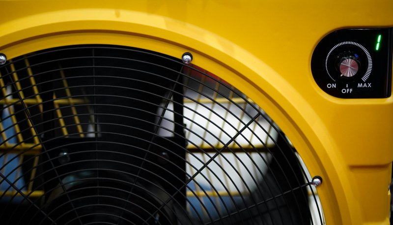 Yellow industrial fan with control dial and protective grille, an air-mover style unit similar to those rented on water mitigation jobs