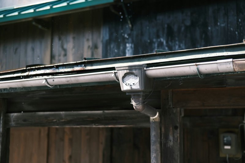 Metal seamless gutter with downspout outlet and decorative cap attached to a wooden building