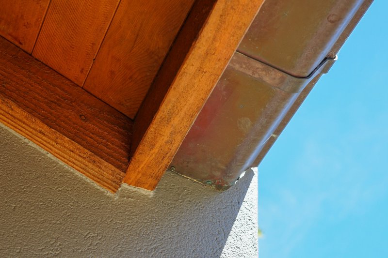 Copper gutter with greenish-brown patina mounted along a wooden eave