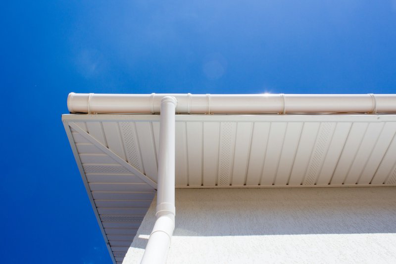 White seamless aluminum gutter and downspout mounted along a building roofline against a clear blue sky