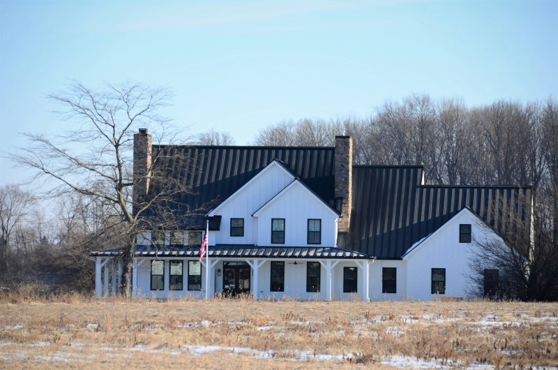 White farmhouse with black corrugated metal roof and stone chimneys