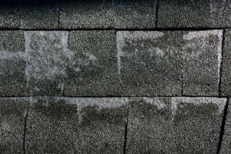 Close-up of weathered dark gray asphalt shingles with granule loss and aging patterns, the kind of roof that should be torn off rather than overlaid