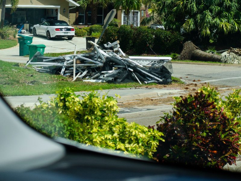Suburban house with a blue tarp covering storm-damaged roof and debris piled by the curb