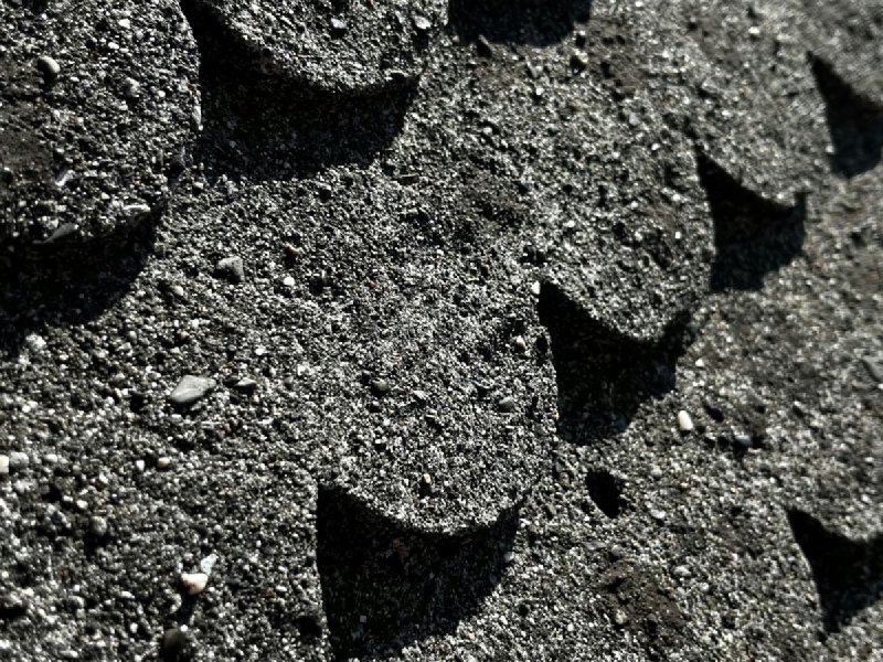 Close-up of black asphalt shingles showing the embedded granules and texture that vary lot to lot