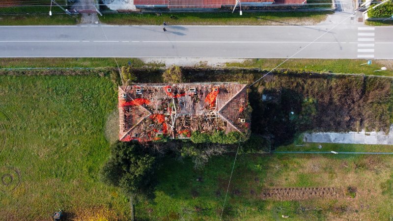 Aerial view of a storm-damaged roof with red netting holding sections in place