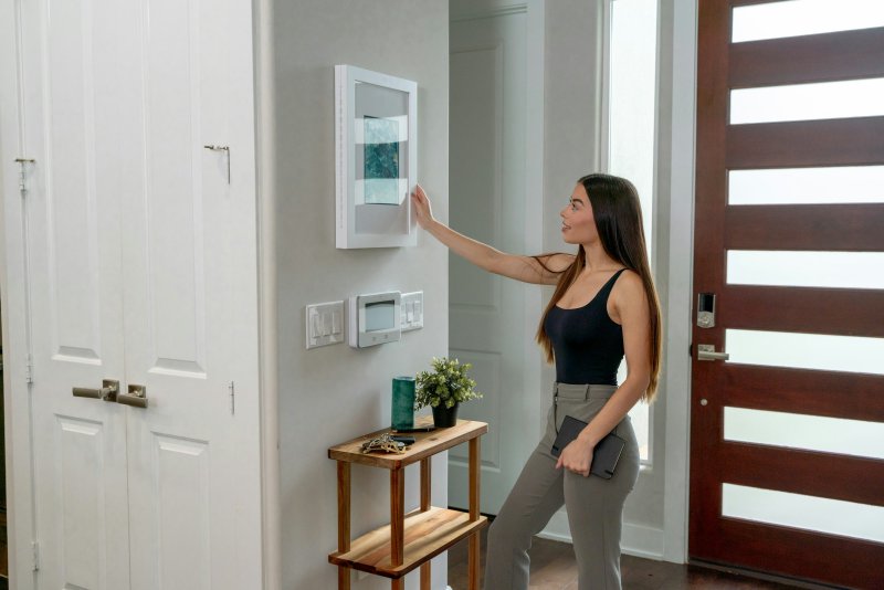 Woman interacting with a wall-mounted smart home control panel near an entryway